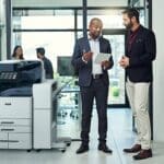 Deux hommes dans un bureau discutent sur une tablette à côté d'une imprimante multifonction couleur Xerox® AltaLink® série C8200 Deux hommes dans un bureau discutent sur une tablette à côté d'une imprimante multifonction couleur Xerox® AltaLink® série C8200