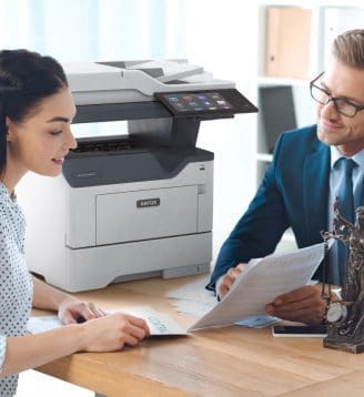 Un homme et une femme assis &agrave; une table, engag&eacute;s dans une conversation tandis qu'une imprimante Xerox&reg; est positionn&eacute;e &agrave; proximit&eacute;.