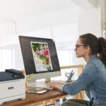 Une femme assise à un bureau, concentrée sur son travail, avec une imprimante Xerox® C320 couleur Une femme assise à un bureau, concentrée sur son travail, avec une imprimante Xerox® C320 couleur