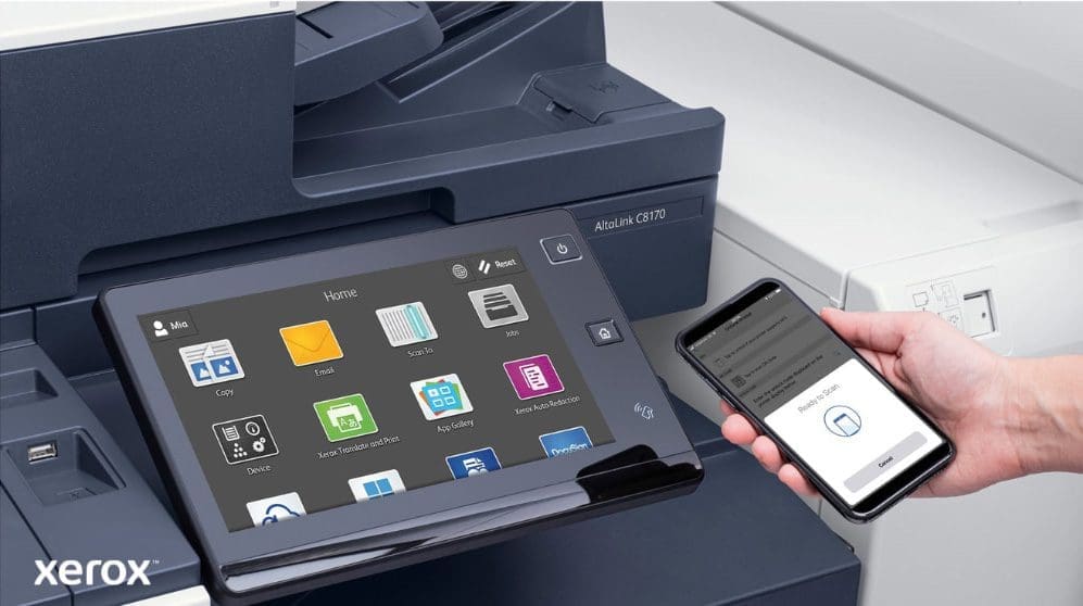 Gros plan de la main d'une personne tenant un smartphone, qui est connect&eacute; sans fil au panneau de commande &agrave; &eacute;cran tactile d'une imprimante multifonction Xerox, mettant en valeur les capacit&eacute;s d'impression et de num&eacute;risation mobiles transparentes de Xerox ConnectKey.