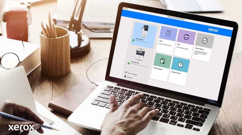 Les mains d'une personne sont pos&eacute;es sur un clavier d'ordinateur portable et l'&eacute;cran affiche l'interface Xerox Print and Scan Experience avec des options telles que Num&eacute;riser, Imprimer, &Eacute;tat de l'appareil, Commander des fournitures et Centre d'assistance, indiquant un contr&ocirc;le convivial.