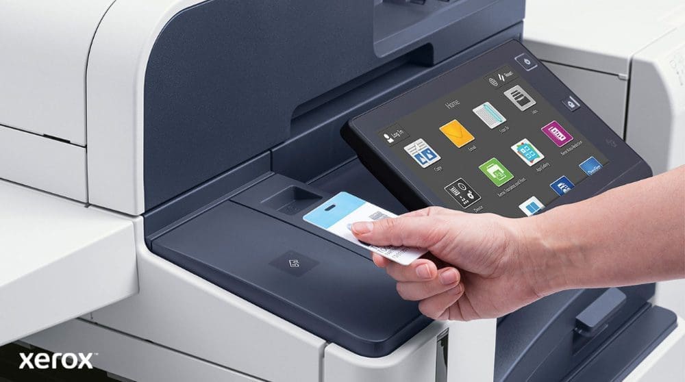 Une main tient une carte de s&eacute;curit&eacute; et la scanne pr&egrave;s du lecteur de carte d'une imprimante multifonction Xerox moderne dot&eacute;e d'un grand &eacute;cran tactile affichant diverses ic&ocirc;nes d'application.